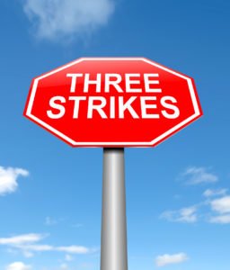 Sign that says "Three Strikes" against blue sky
