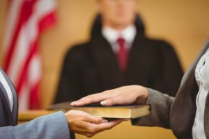 closeup of witness placing hand on bible before testifying