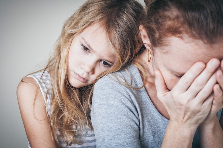 Mom looking sad with young daughter leaning on her
