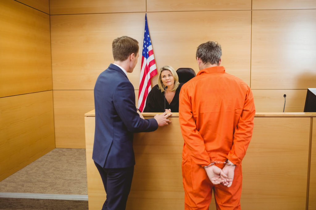 Judge, defense attorney, and defendant in orange jumpsuit during 72-hour hearing.