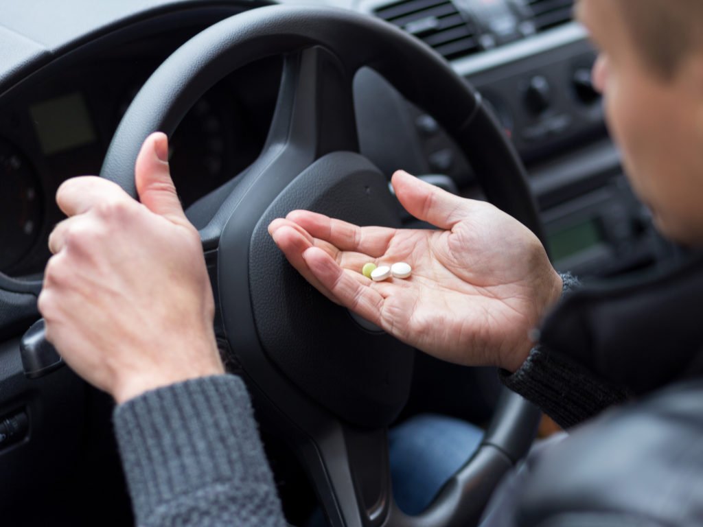 Conductor sosteniendo pastillas con una mano en el volante