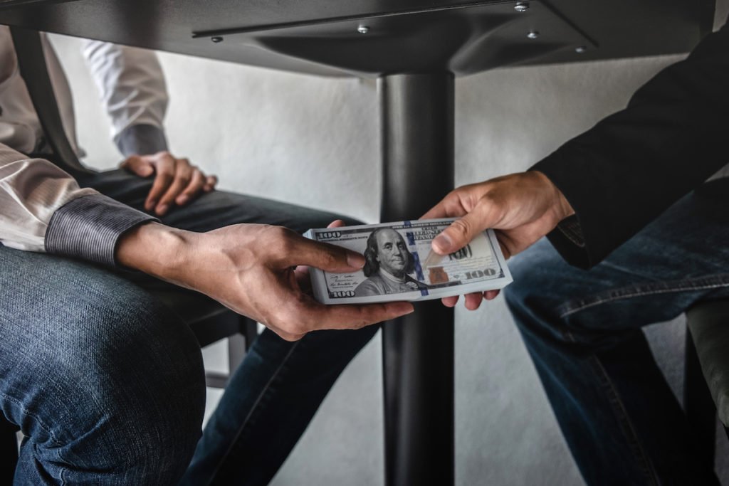 Man handing stack of $100 bills under the table as an example of being an accessory after the fact