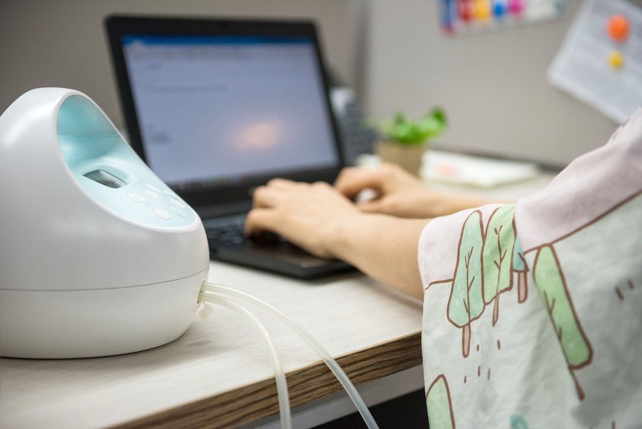 Máquina de extracción de leche en la mesa de trabajo mientras la madre está escribiendo en la computadora