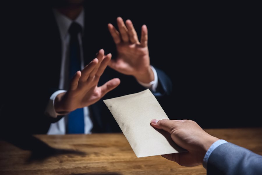 Una mano ofreciendo un sobre con dinero a otra persona, quien lo rechaza con un gesto de la mano