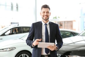 Car salesman smiling in front of sedan
