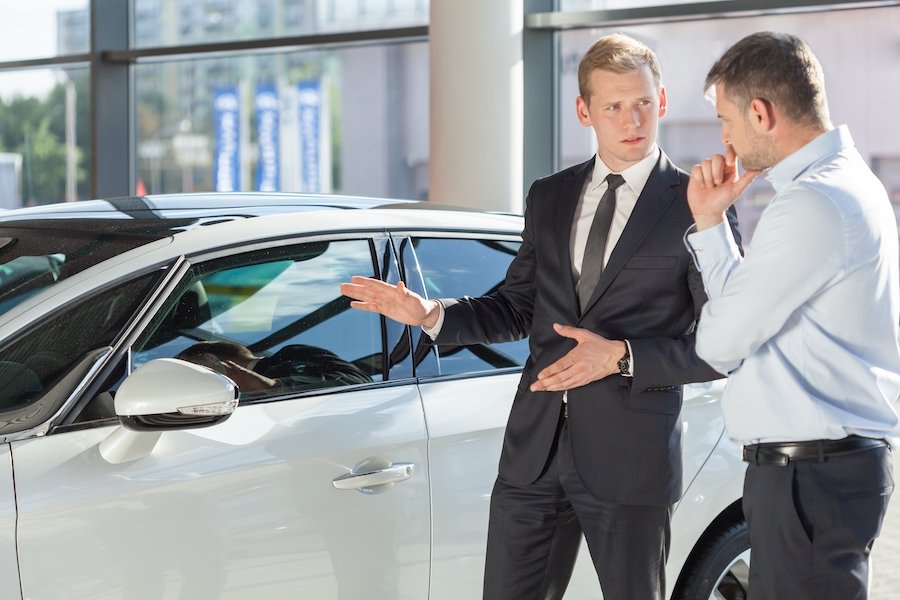 Car salesman with customer in front of sedan