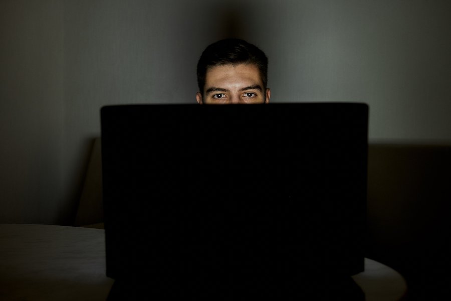 Hombre mirando una computadora portátil que presumiblemente contiene pornografía infantil en violación de CRS 18-6-403, y la habitación está oscura e iluminada solo por la luz de la pantalla de la computadora