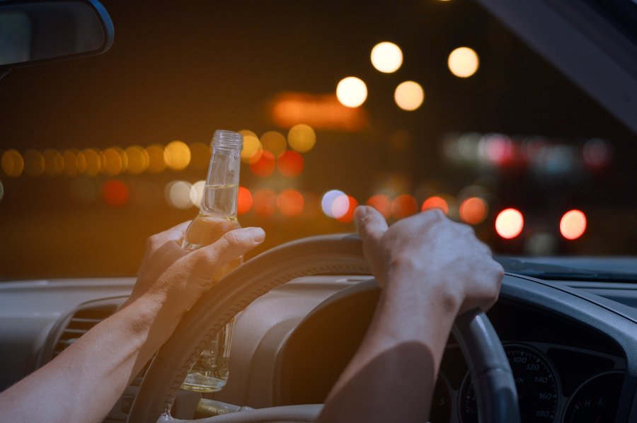 Primer plano de manos en el volante con una sosteniendo una botella de cerveza