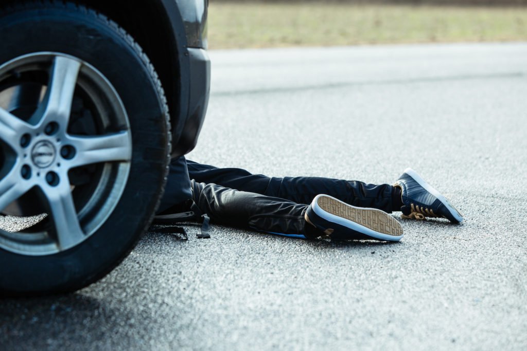 Wheels of car near legs of victim who was just hit on the road - causing an accident with death or serious injury can lead to a DMV fatality hearing