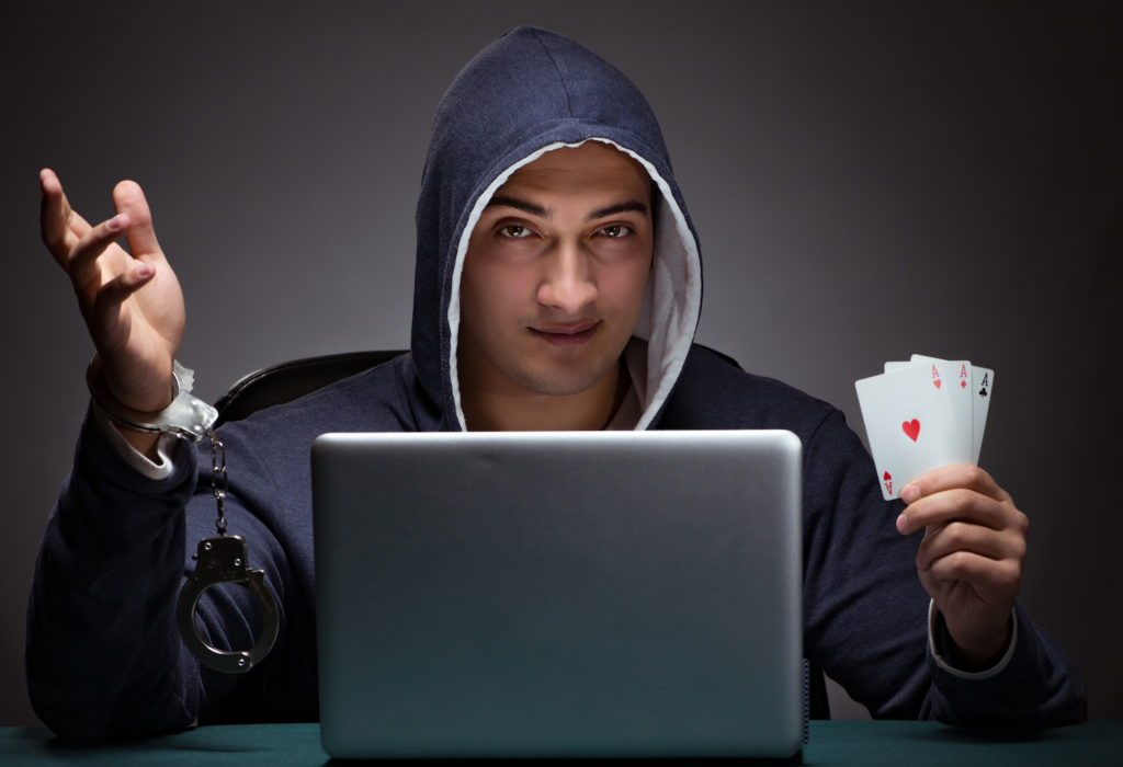 Hooded man behind laptop with cards violating CRS 18-10-106.