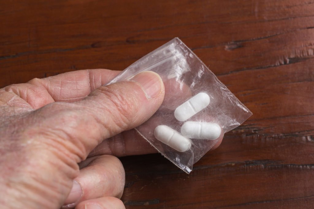 Closeup of hand holding baggie with three hydrocodone pills