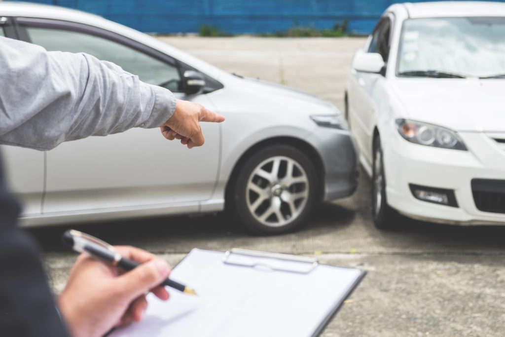 Colisión de automóvil en segundo plano con conductor hablando con un ajustador de seguros en primer plano