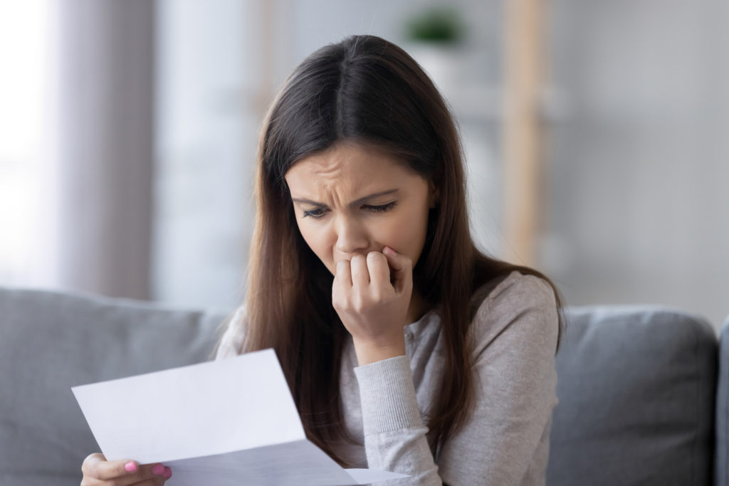 Woman on couch reading a letter looking distraught 