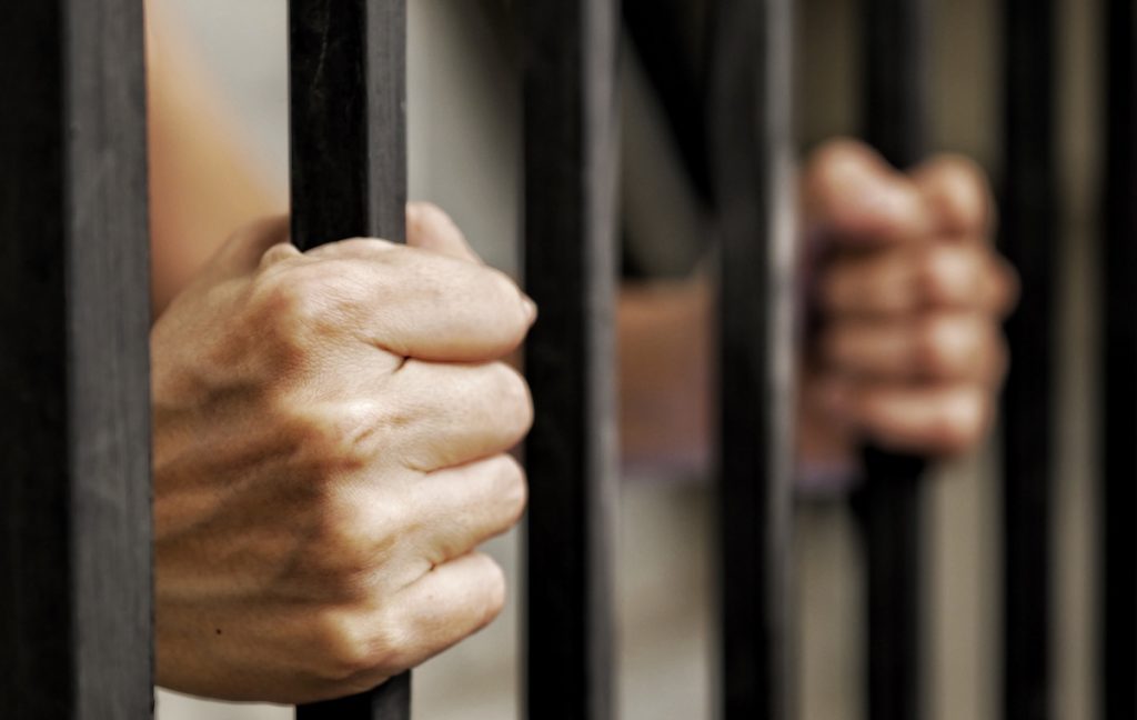 Recluso en celda de prisión agarrando los barrotes - El Código Penal de California 32 PC es castigado con hasta 3 años de custodia
