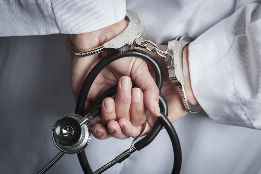 Primer plano de las manos de los médicos sosteniendo un estetoscopio con esposas después de una violación del Código de Negocios y Profesiones 2052