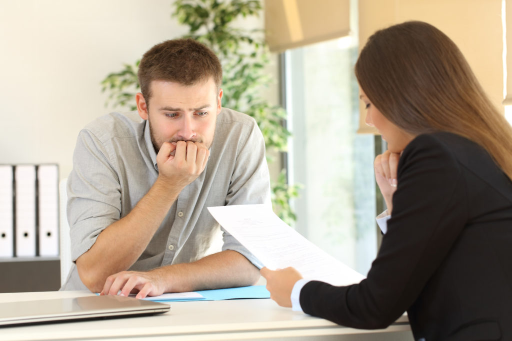 Nervous-looking employee talking to manager during a meeting as the manager looks at some documentation