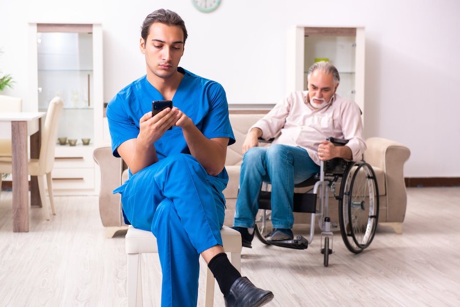 Personal de hogares de ancianos mirando el teléfono celular e ignorando a un residente en silla de ruedas detrás de él