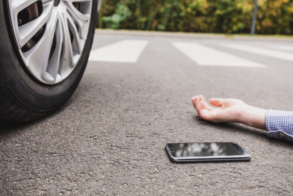 Close up of pedestrian victim's hand on ground next to cell phone with car tire nearby