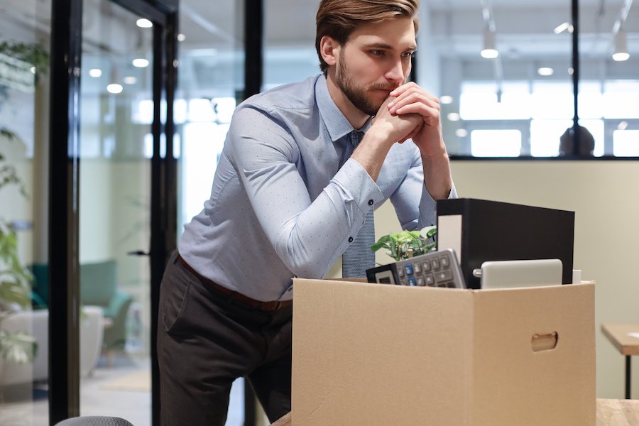 Fired worker leaning on box of belongings from office