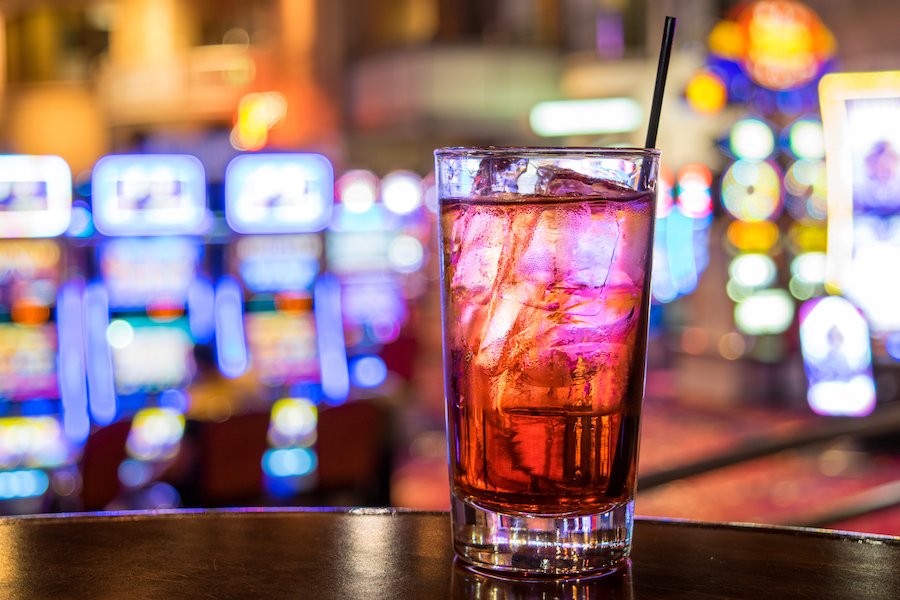 Vaso de alcohol con máquinas tragamonedas de casino en segundo plano