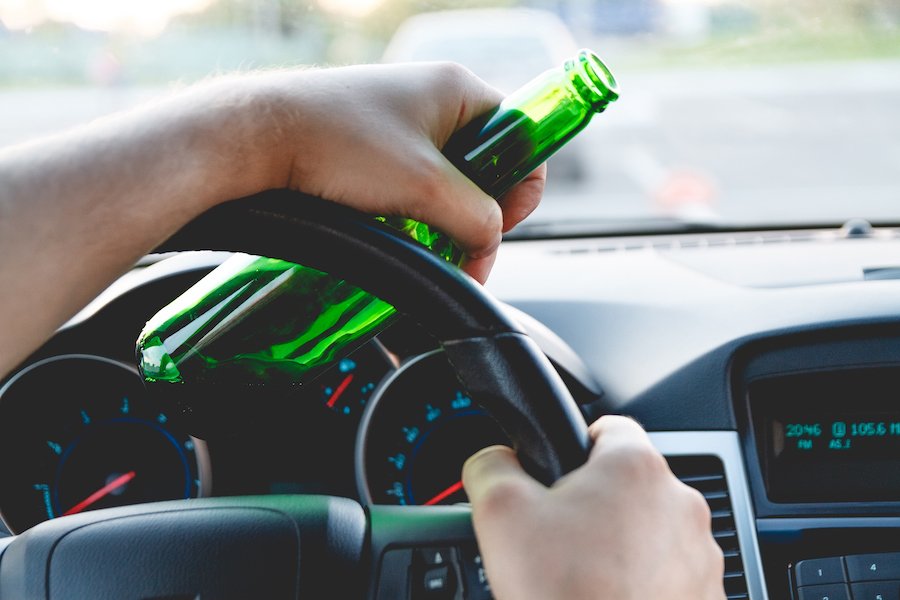 Hand holding steering wheel and bottle of beer as an example of misdemeanor DUI