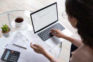 Employee compiling expense reports on her laptop, and her desk is holding a cup of coffee and a plant