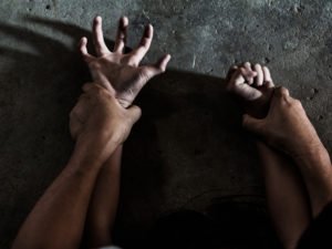 Primer plano de manos masculinas sosteniendo violentamente las manos femeninas por las muñecas contra el suelo durante una agresión sexual en violación de la NRS 200.366