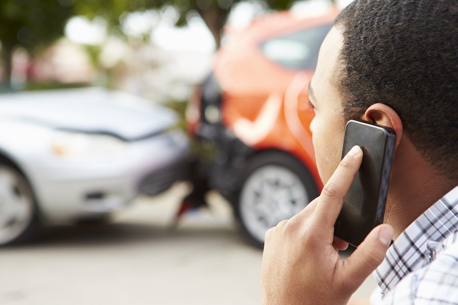 Driver calling insurance company on clel phone while looking at car accident aftermath