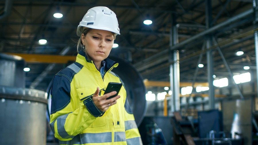 Trabajador con casco de seguridad sosteniendo un teléfono celular - muchos estados, incluyendo California, requieren reembolsos por el uso comercial de sus teléfonos celulares personales