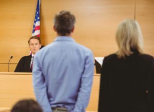 Corte reprendiendo al acusado (parado junto a su abogado defensor) por no presentarse en la corte