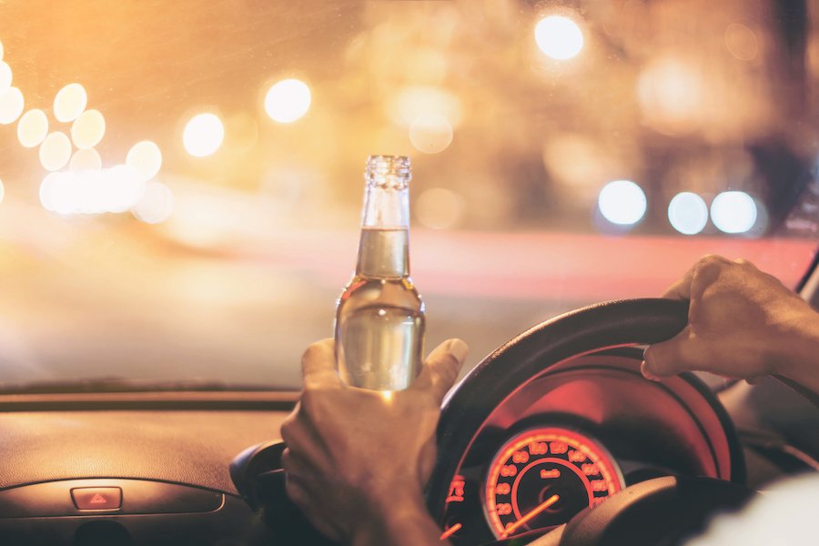 Mano en el volante con la otra mano sosteniendo una botella de cerveza