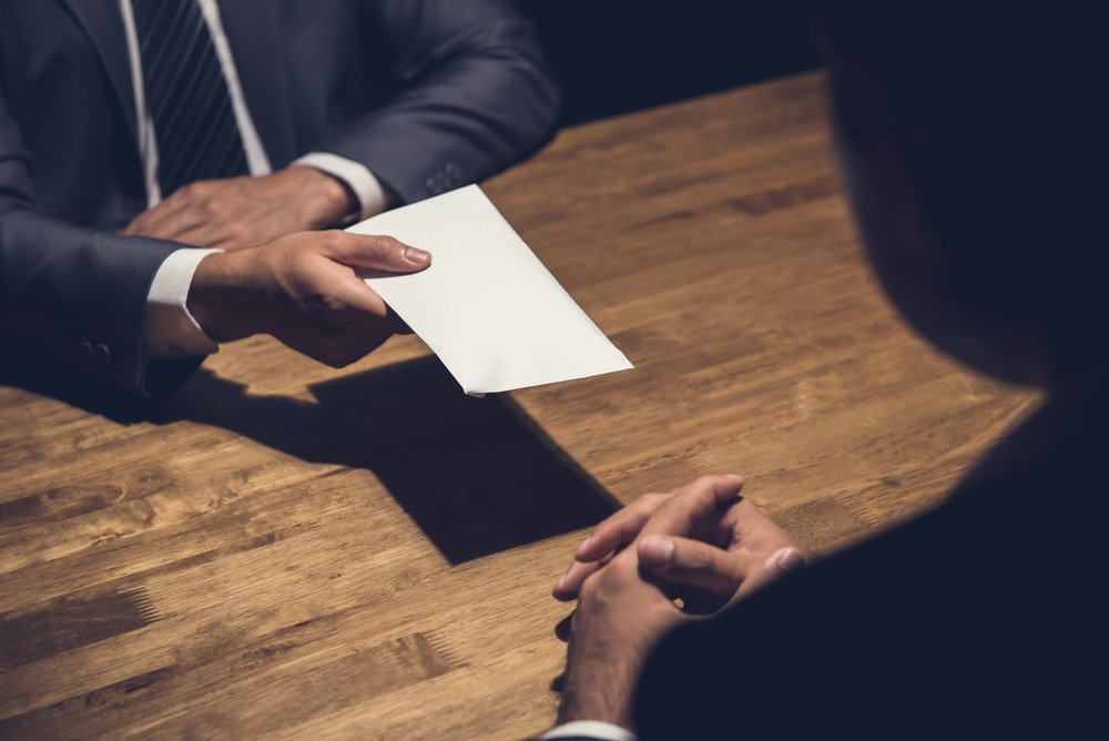 man handing off an envelope filled with money to another