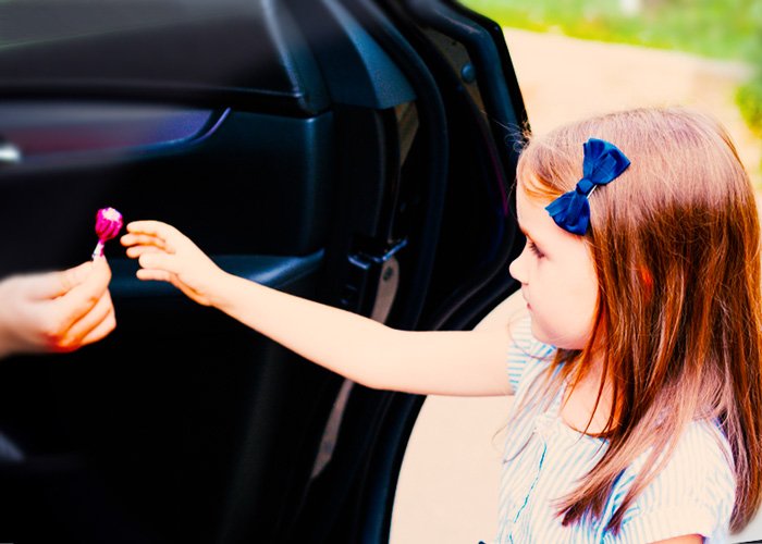 girl reaching out for a lollipop from a stranger in a car