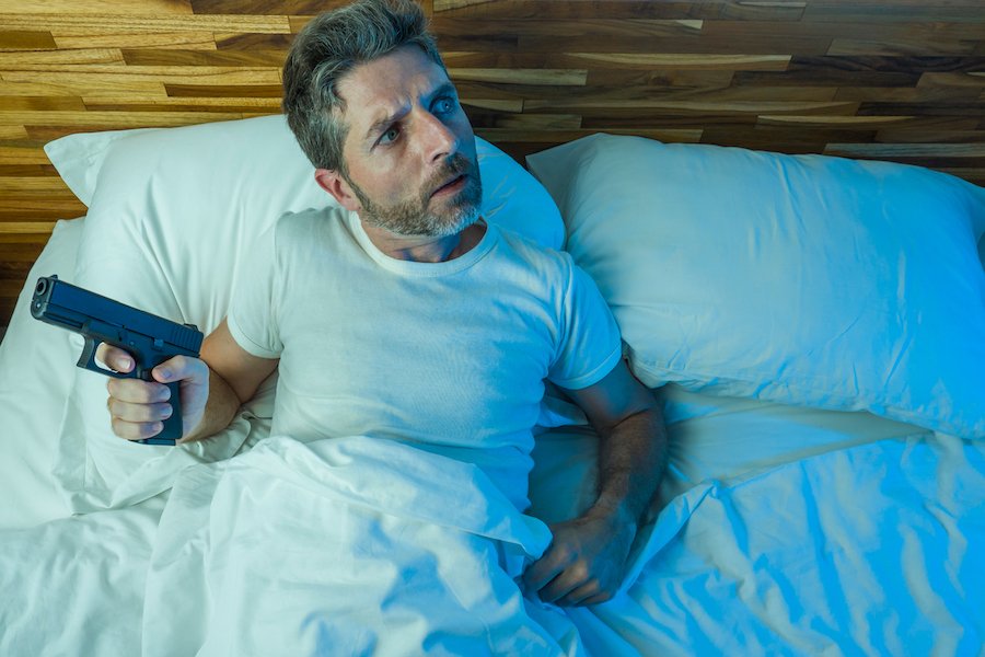 Hombre en la cama sosteniendo un arma escuchando a un intruso en la casa como ejemplo de donde la ley Make My Day de Colorado podría aplicar