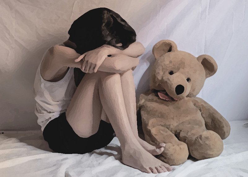 child hunched over next to teddy bear