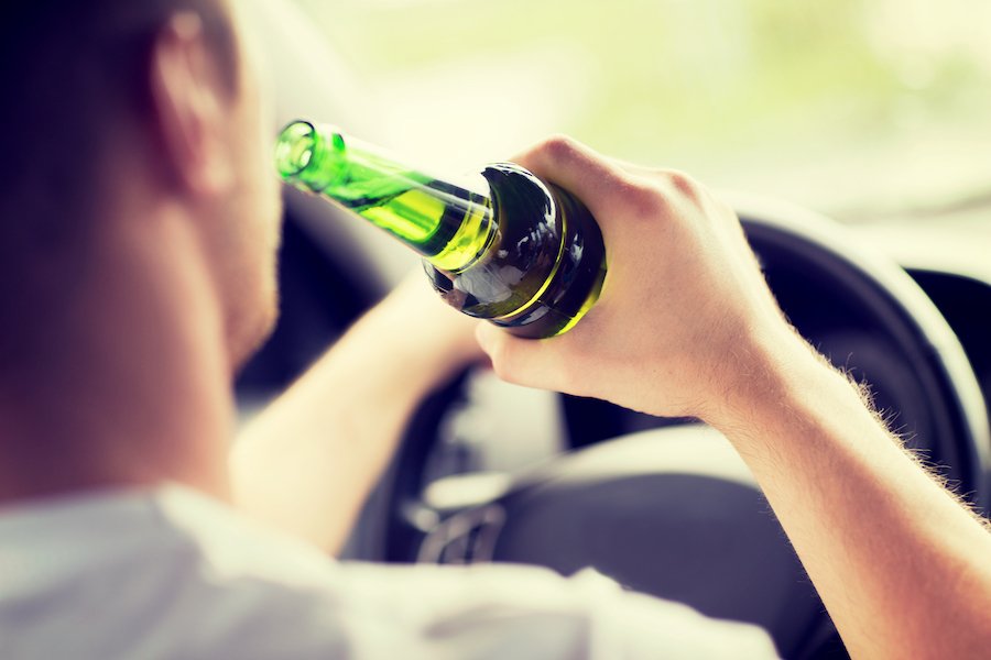 Conductor sosteniendo botella de cerveza mientras la mano está en el volante