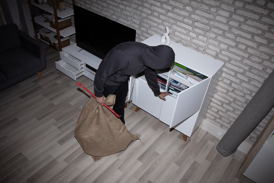 Thief in hoodie with crowbar looking through cabinet