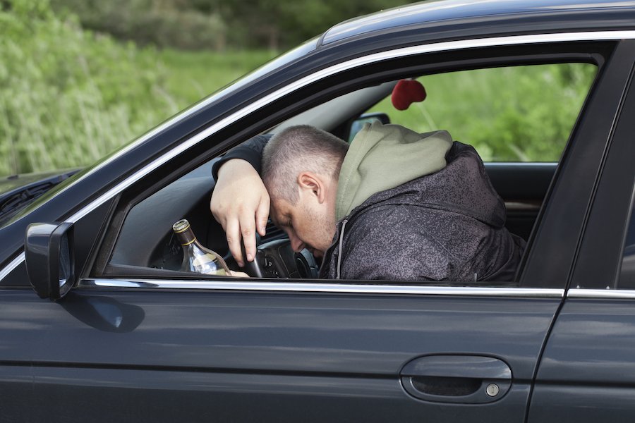 Drunk man passed out over steering wheel with beer bottle