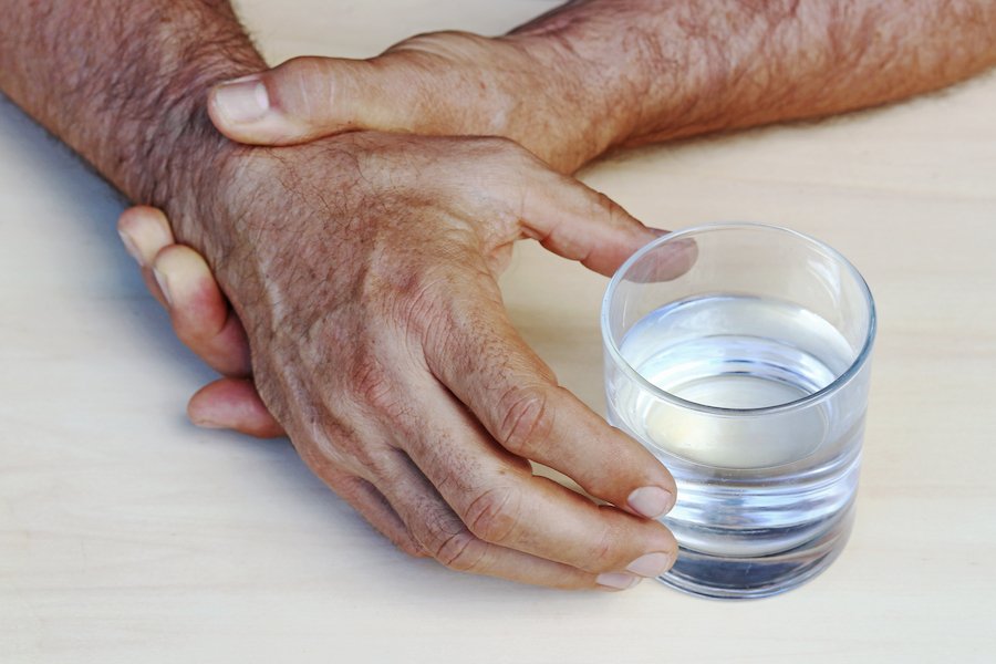 Hand or Parkinson's patient struggling to grasp water glass