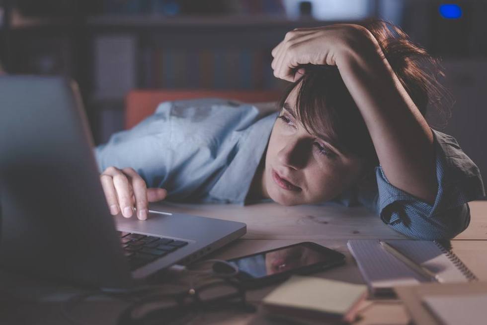 Empleado cansado frente a la computadora por la noche que puede tener derecho a horas extras bajo la ley de horas extras de California por trabajar horas extras