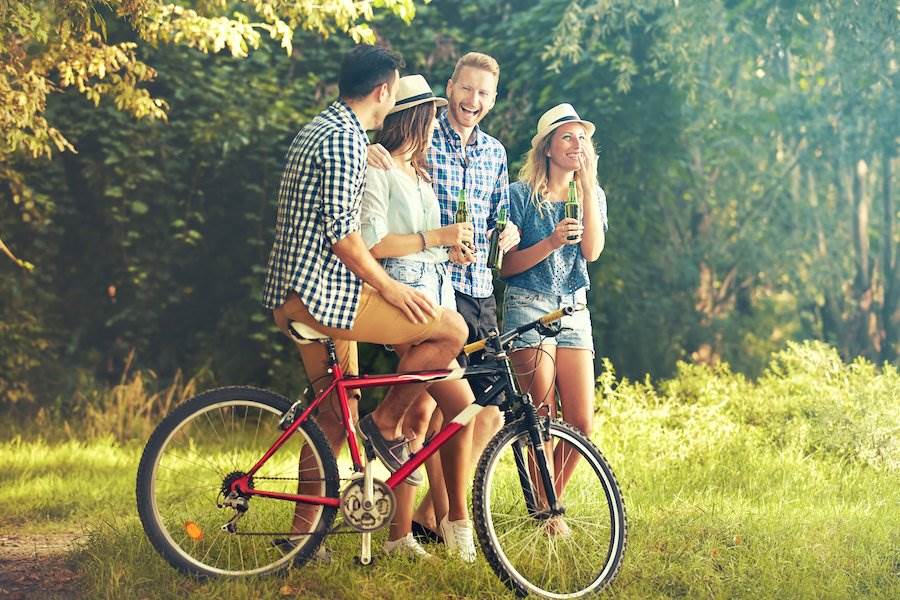 Persona en bicicleta con amigos sosteniendo cervezas