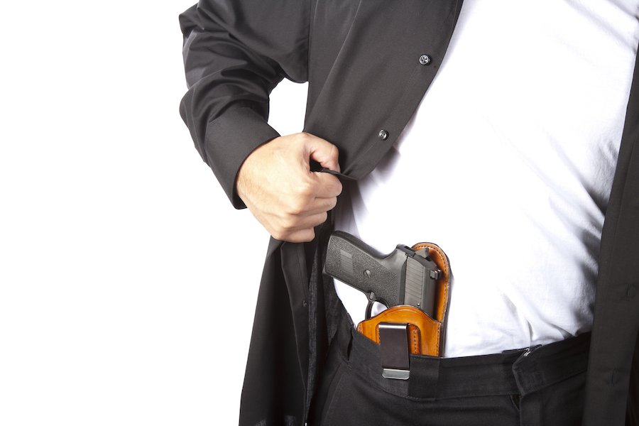 Hombre tirando de la camisa para revelar una pistola metida en los pantalones