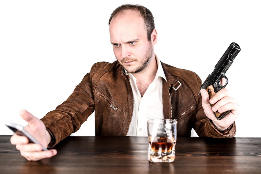 Drunk man at bar holding gun with alcohol in front of him