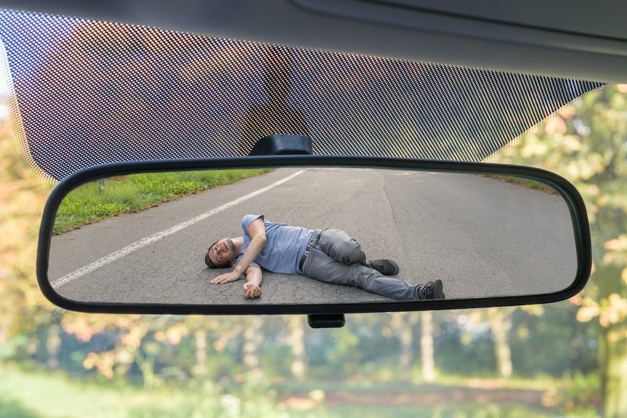 Adult pedestrian lying injured on the road after being hit by car, as seen through its rear-view mirror