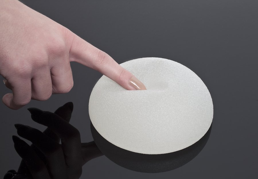 Textured breast implant being poked by lady's finger on table