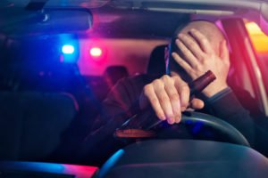 Upset male driver is caught driving under alcohol influence. Man covering his face from police car light.