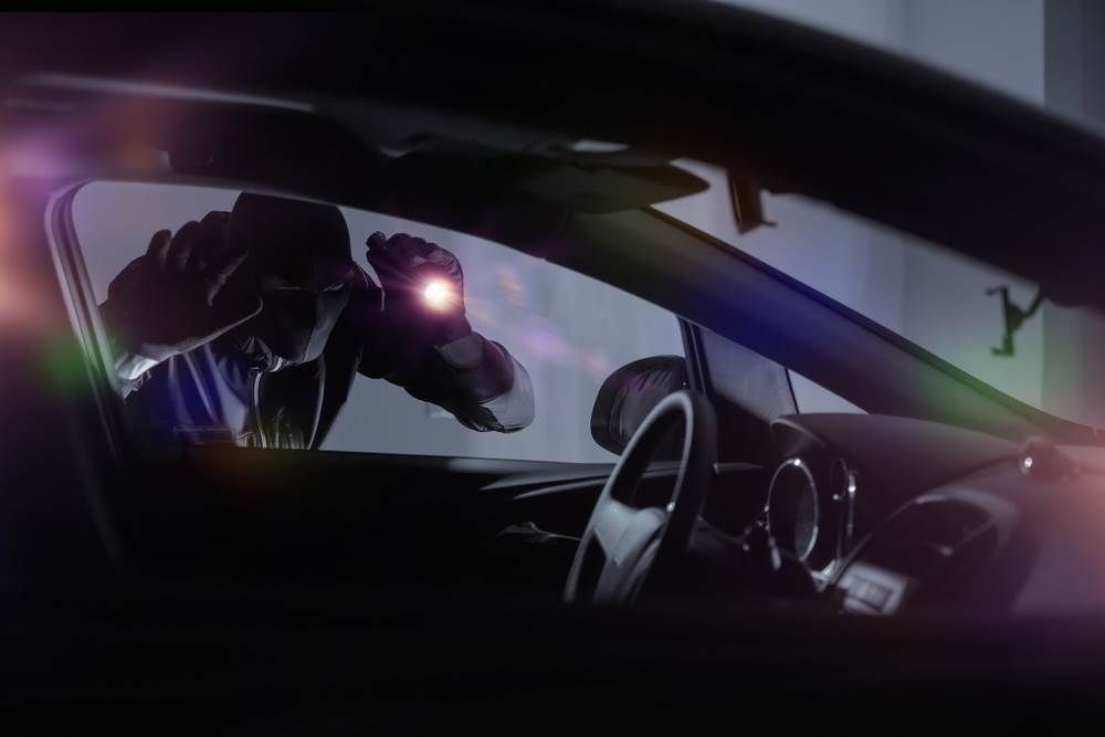 Masked man shining light inside car.