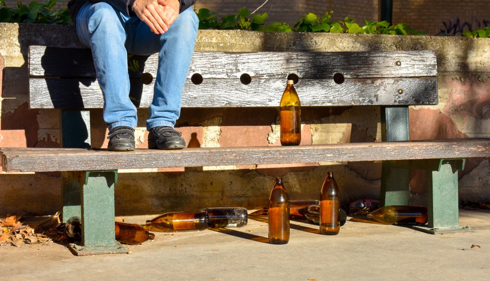 Person sitting at bench with multiple empty bottles of alcohol.