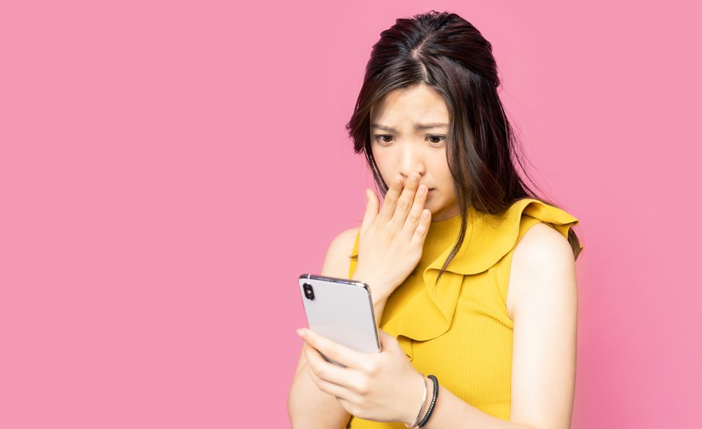 Una joven sorprendida, con la mano sobre la boca mientras mira su teléfono celular.