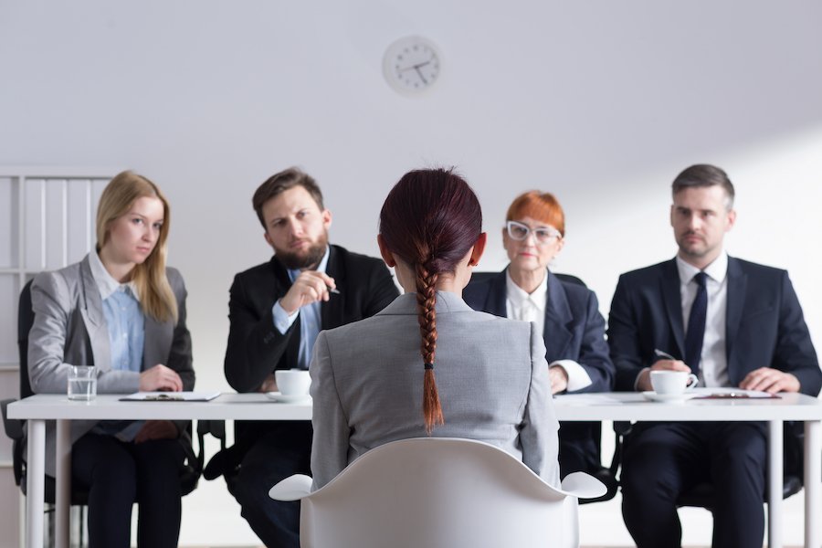 Cuatro personas en trajes de negocios en una mesa de reuniones entrevistando a un candidato a un trabajo sentado en una silla frente a ellos